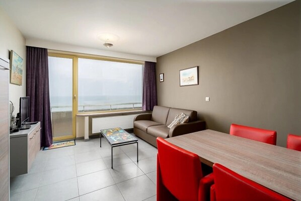 A modern living room with a sofa, a dining table, and a view of the sea through large windows. - Stone Home in Dordogne Near Prehistoric Caves (Blankenberge)