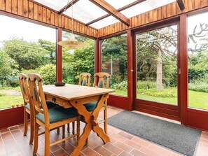 A conservatory with a wooden table and chairs, a hanging light fixture, and a view of a garden through large glass doors. - 10 Person Holiday Home in Spottrup (Spøttrup)