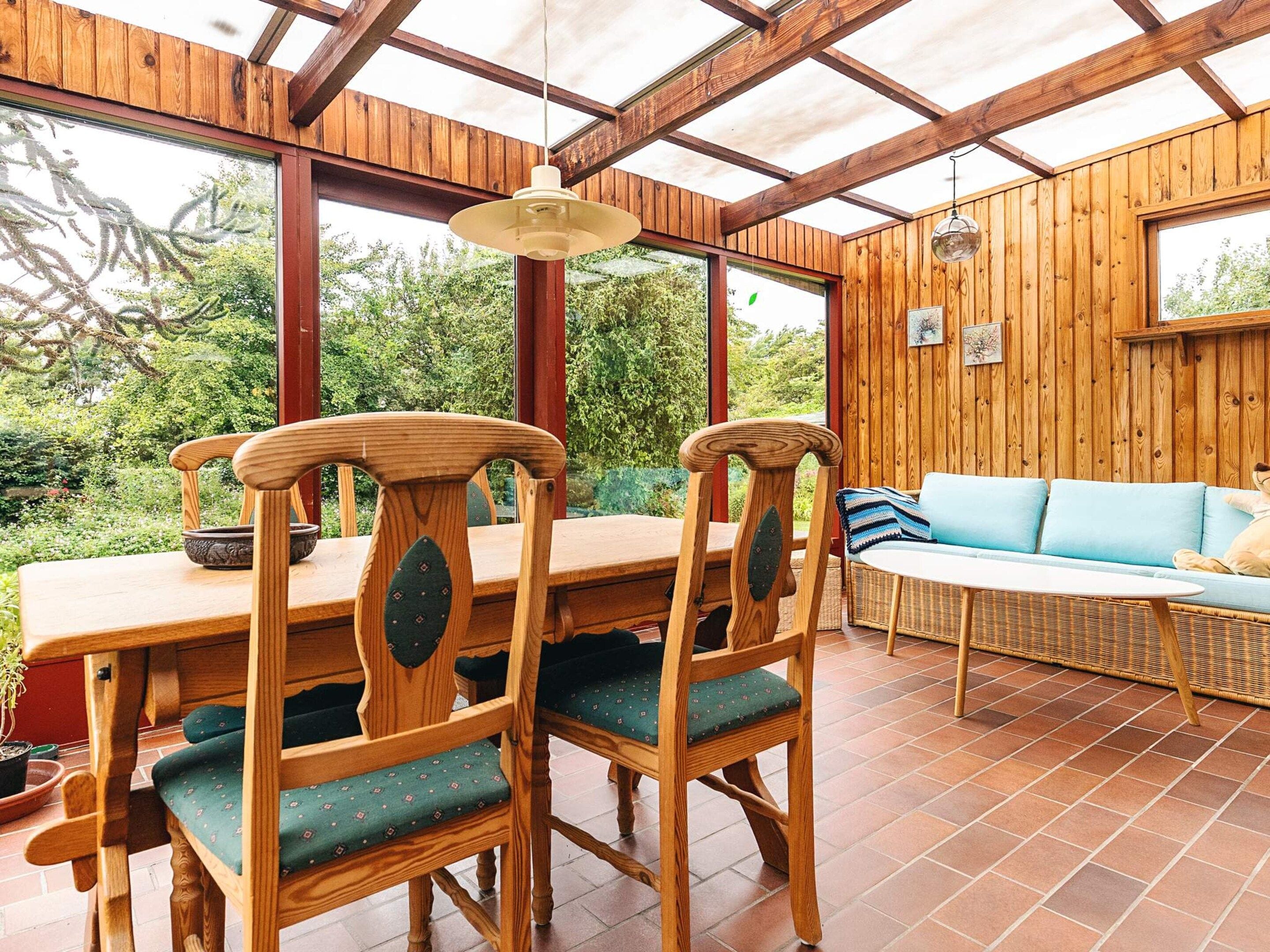 Interior em madeira com uma mesa de jantar e cadeiras, um sofá e um lustre.
