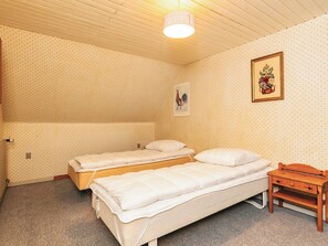 A room with two single beds, a wooden nightstand, a wall-mounted light fixture, and a framed picture.
