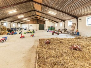 A spacious barn with a high ceiling, various farming equipment, and hay bales.