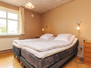 Ein Schlafzimmer mit einem Doppelbett, einem Nachttisch, einer Lampe, einem Fenster mit Vorhängen und einer Heizung.