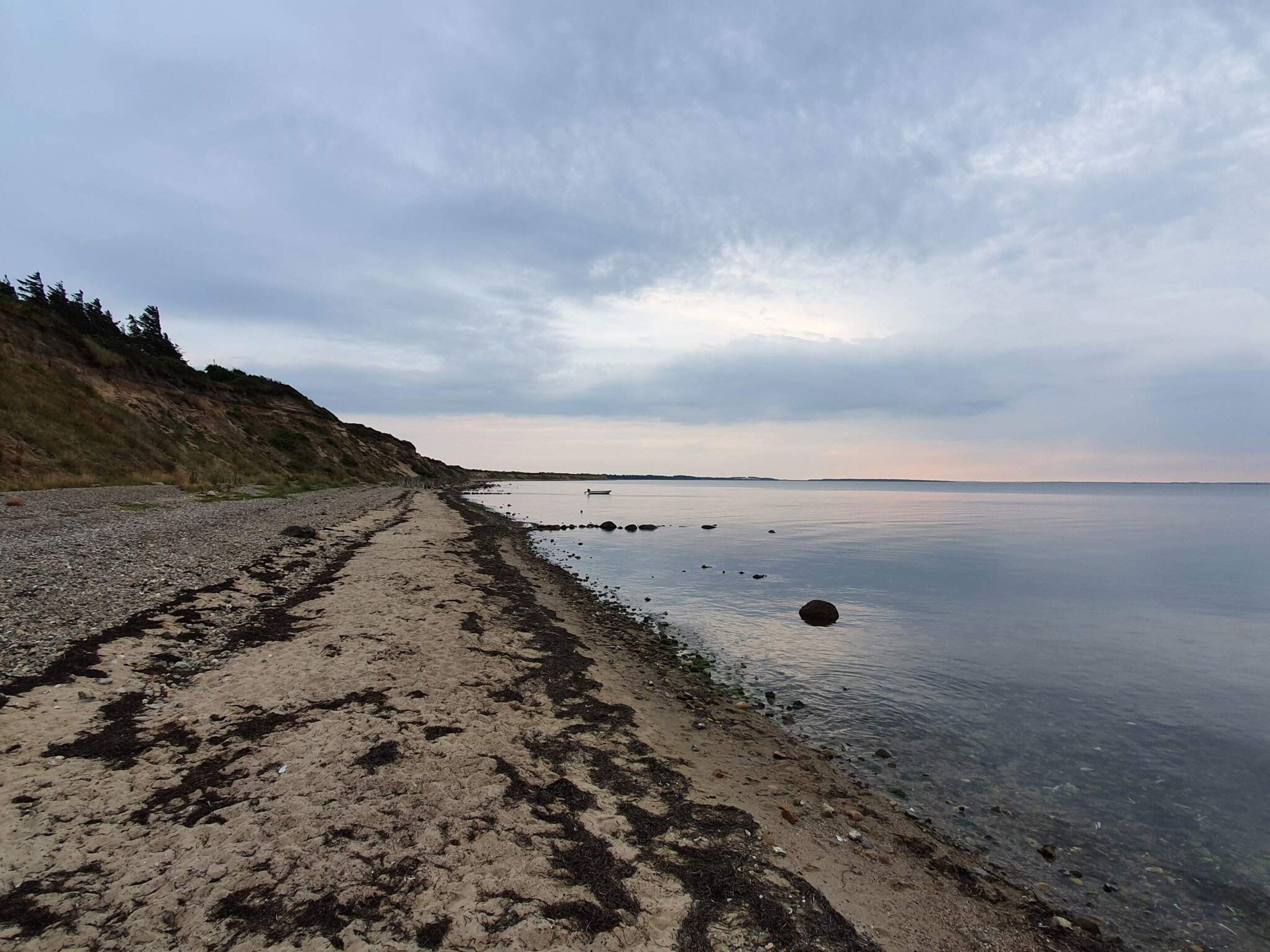 A beach with a clear path leading to the water, surrounded by hills.