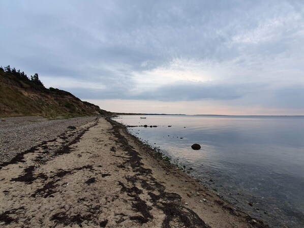 A beach with a clear path leading to the water, surrounded by hills.