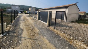 A gravel driveway leading to a gated area with a building that has a tiled roof and a garage. - Maison Noé ( New Villa ) Spacious near the center Fully air-conditioned (Ruoms)