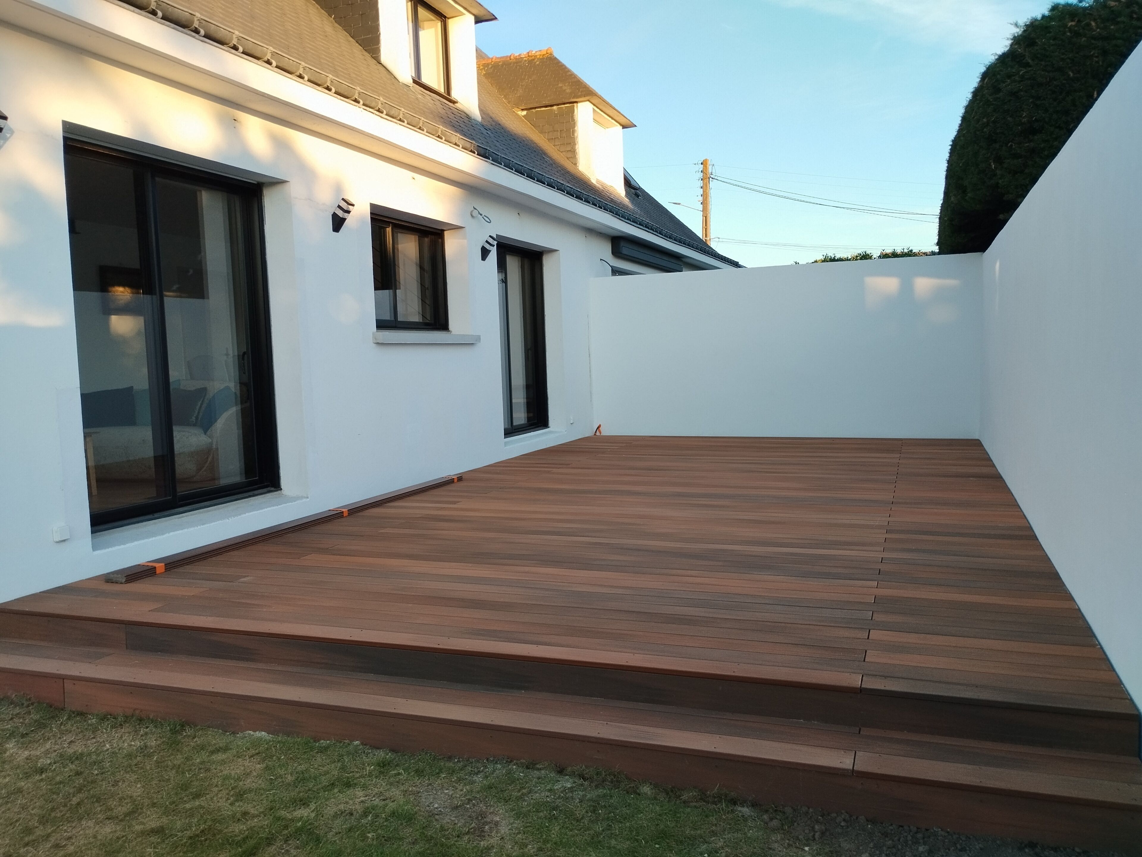 Una casa moderna con terraza de madera, ventanas grandes y fachada blanca.