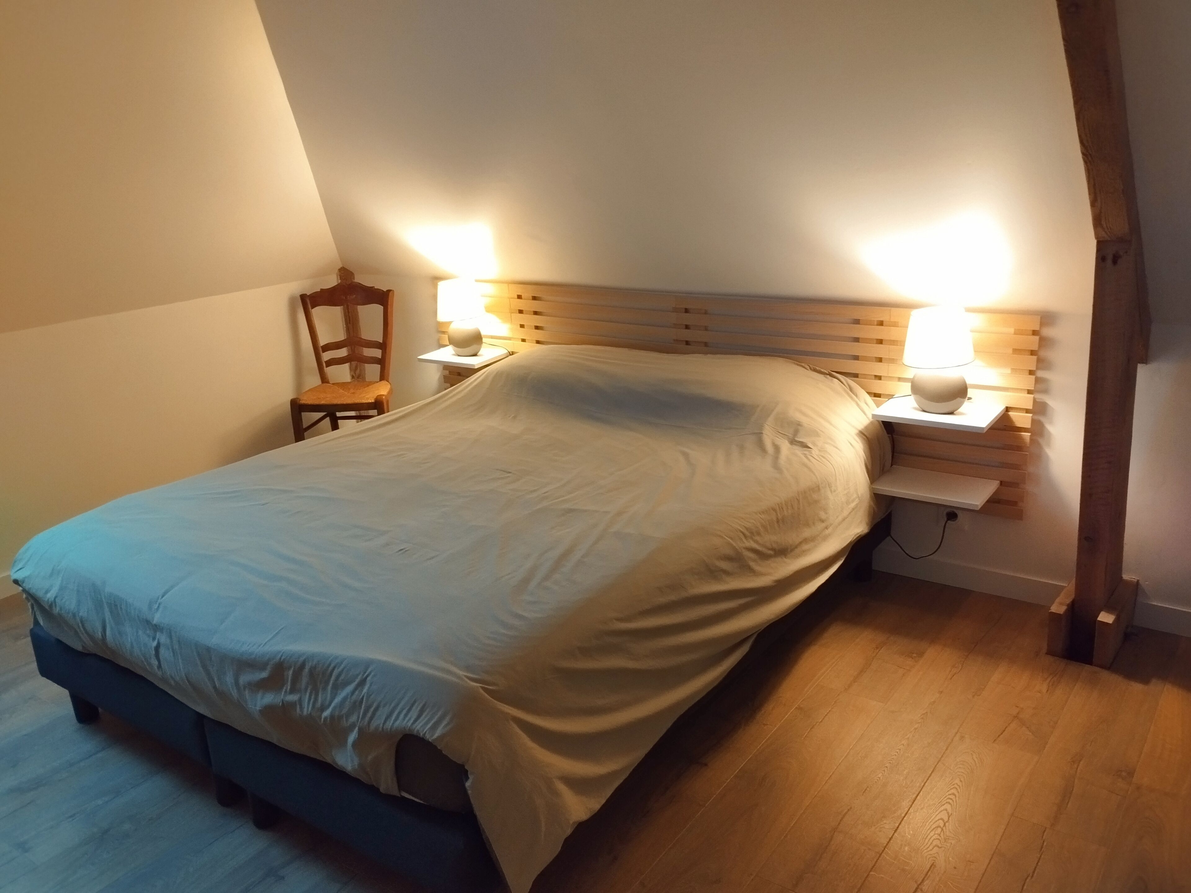 Une chambre à coucher avec un lit, deux lampes de chevet, une chaise et une tête de lit en bois.