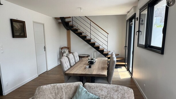 A modern living room with a sofa, a dining table, and a staircase leading to another level. - Quiberonnaise house in town center, walking distance to beach. (Quiberon)