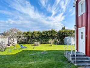 Un edificio rojo con puerta blanca, un espacio cubierto para sentarse al aire libre y un césped cuidado.