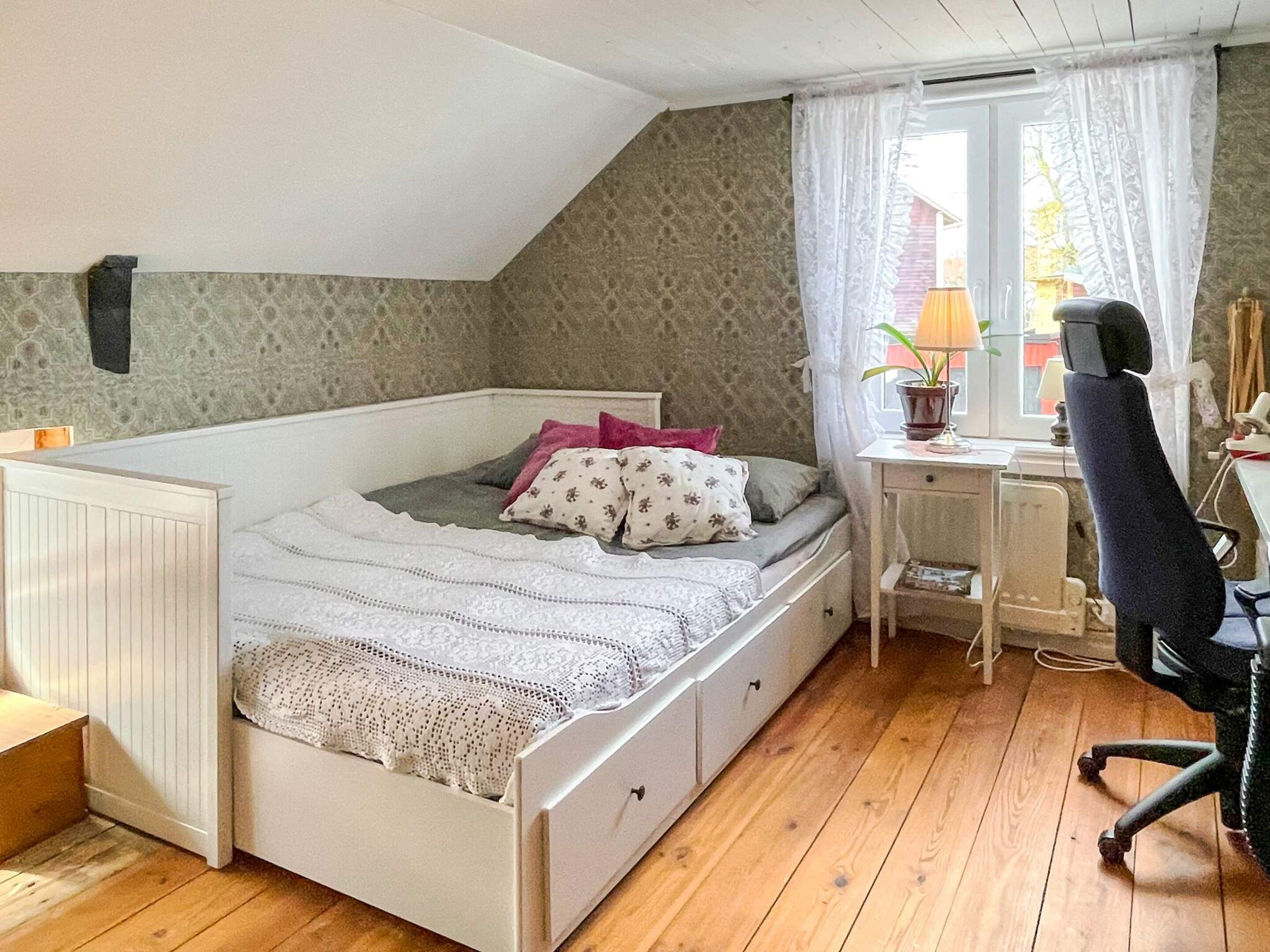 A single-bed room with a desk and chair, a window with curtains, and a radiator.