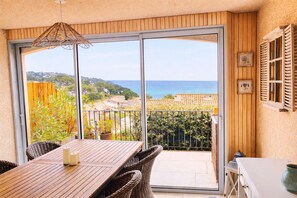 A balcony with a view of the sea, a table with chairs, and a hanging light fixture.