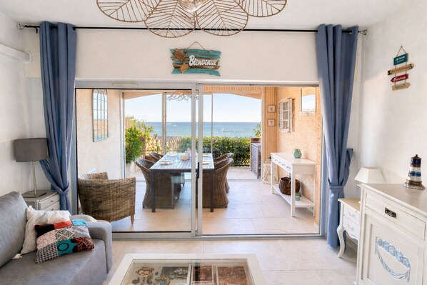 A room with a view of the sea, a dining area with wicker furniture, and a white dresser.