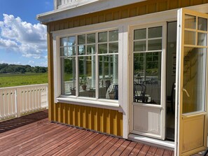 A wooden deck with a white railing, a glass door, and a view of a green landscape. - 5 Star Holiday Home in Askeron (Hjaelteby)