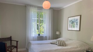 A bedroom with a bed, a chair, a lamp, a window with sheer curtains, and a framed picture on the wall. - 5 Star Holiday Home in Askeron (Hjaelteby)