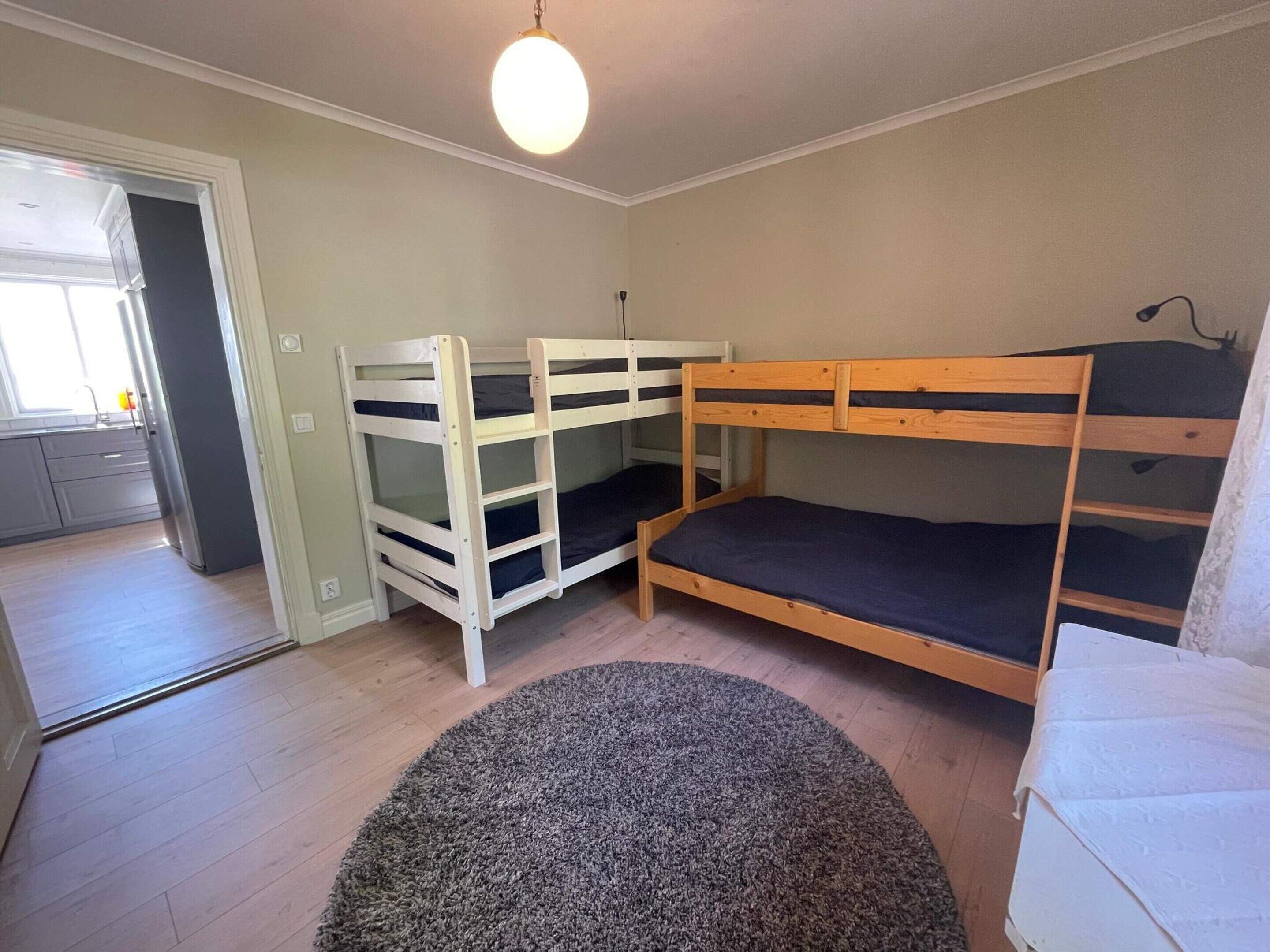Ein Zimmer mit zwei Etagenbetten, einem runden Teppich und einer Tür zu einer Küche.