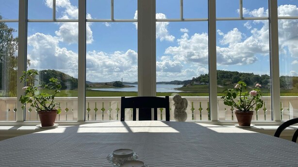 A table with a view of a lake and hills through large windows. - 5 Star Holiday Home in Askeron (Hjaelteby)
