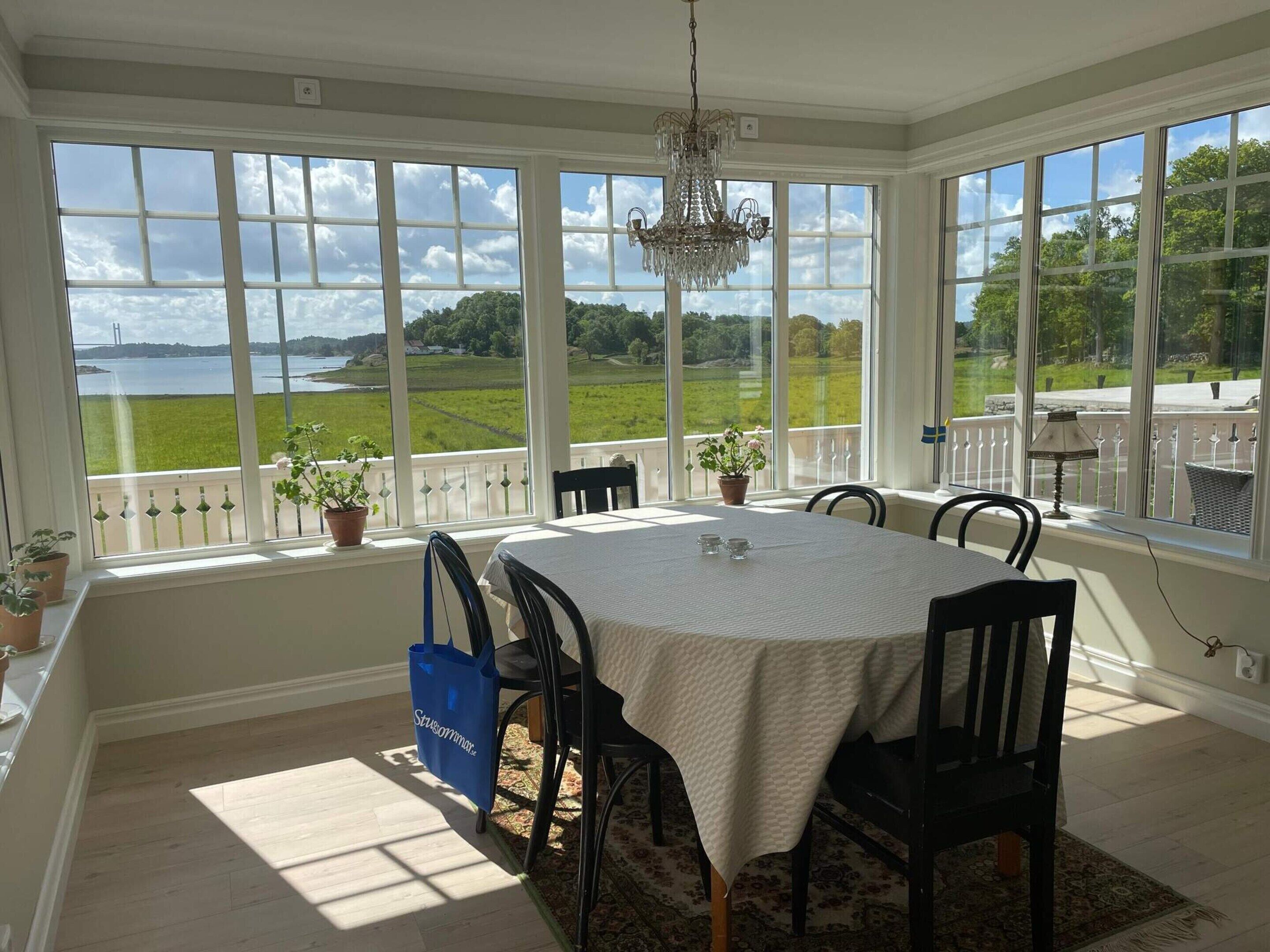 A dining area with a table set for four, large windows offering a view of a green landscape and a body of water.