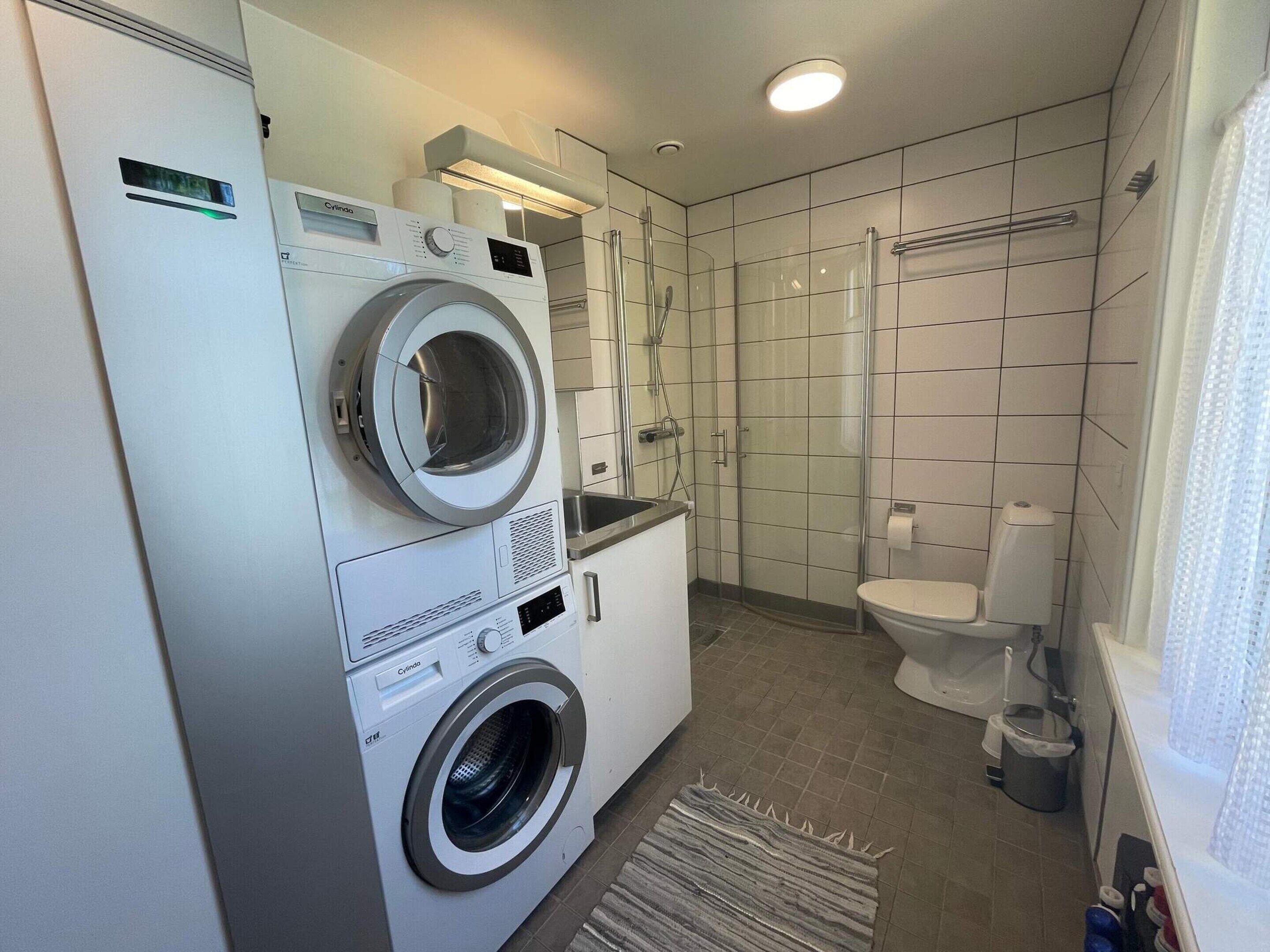Ein kompakter Hauswirtschaftsraum mit einer Waschmaschine und einem Trockner mit Frontlader, einer Duschkabine und einem WC.