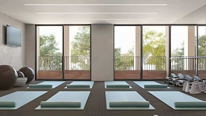 Une salle de sport moderne dotée de grandes fenêtres, de tapis de sol et d’un balcon avec des chaises longues.