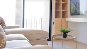Un salon moderne avec un canapé, une petite table sur laquelle est posée une plante, un téléviseur fixé au mur et une porte coulissante donnant sur un balcon.