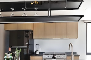A modern kitchen with wooden cabinets, a gas stove, a blender, and wine glasses on the countertop.