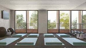 A modern gym with large windows, exercise mats, and a balcony with sun loungers.