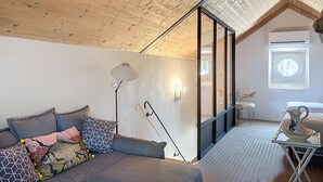 Ett mysigt rum med ett sluttande tak, en soffa med mönstrade kuddar, en golvlampa och ett litet bord med en kanna.