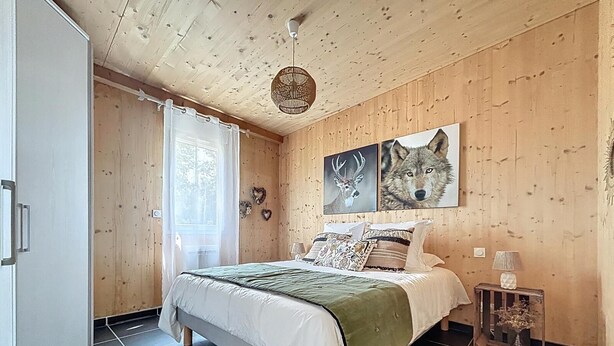 Ett sovrum med träpanel på väggarna, en säng, ett fönster med gardiner och två tavlor med vargmotiv som hänger på väggen.
