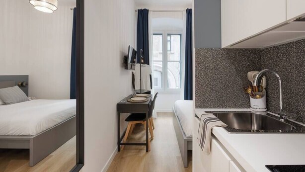 A compact room with a bed, a desk with a chair, a small kitchenette with a sink, and a window with curtains. - Cozy Trieste Historic Hideaway (Trieste)