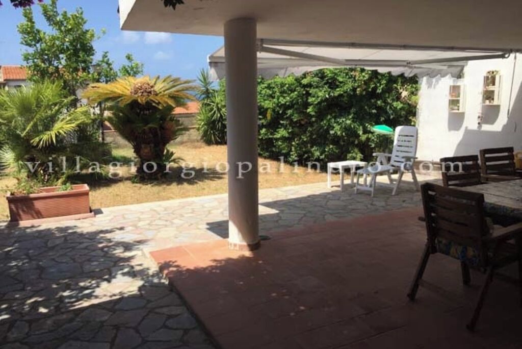 A covered outdoor area with a stone floor, a white column, and a table with chairs.