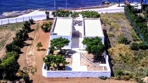 Um imóvel costeiro com um edifício branco, rodeado por vegetação e vista para o oceano.