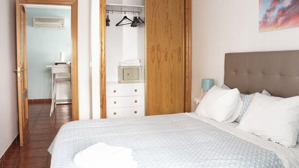 A bedroom with a bed, a wardrobe, a bedside table, and a chair.