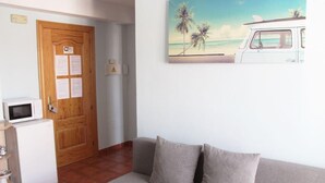 A room with a wooden door, a white refrigerator, a grey sofa, and a beach-themed painting on the wall.
