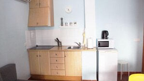 A compact kitchen with wooden cabinets, a microwave, and a small refrigerator.