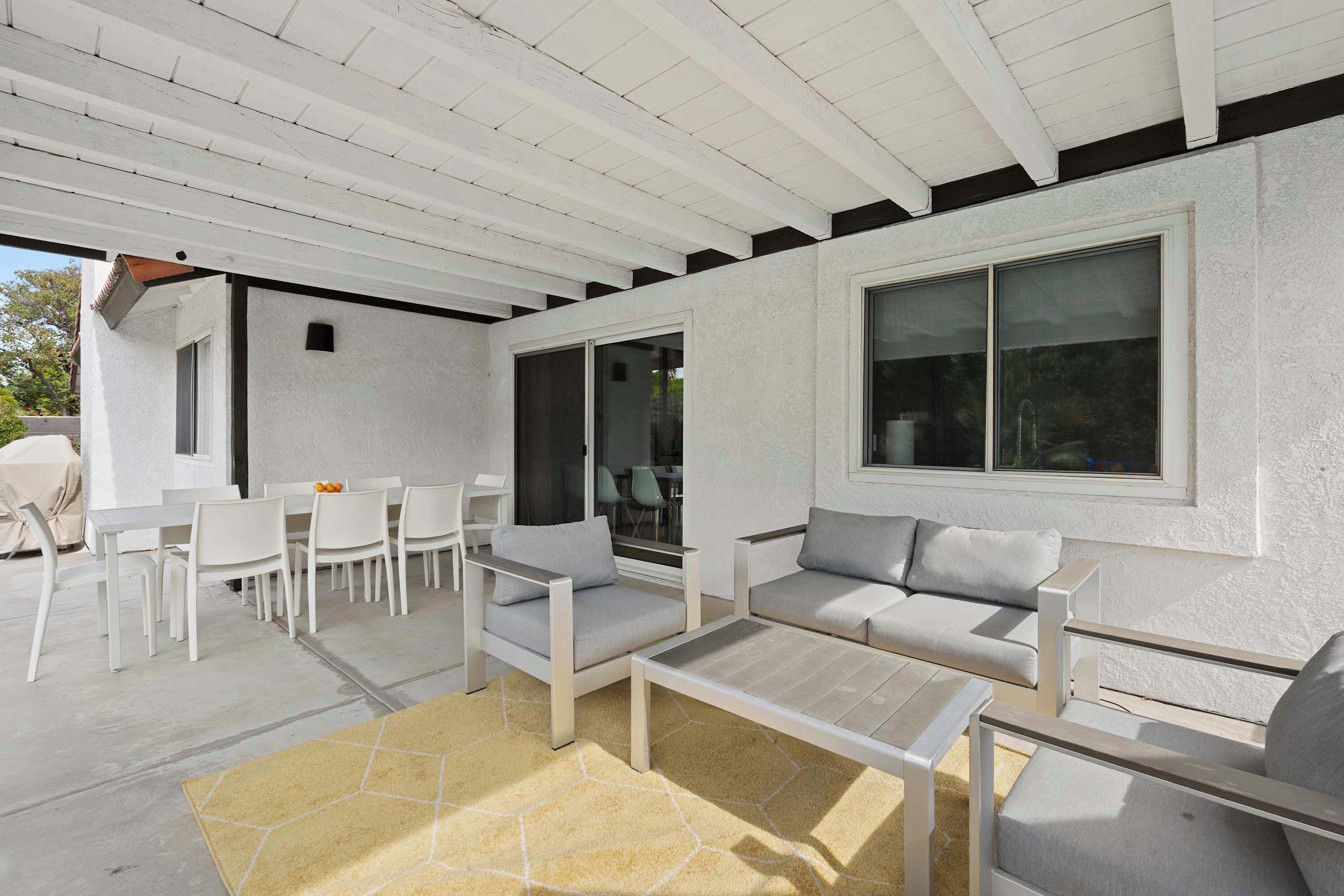 A covered outdoor patio with white furniture, including sofas and chairs, and a dining table.
