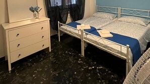 A bedroom with two beds, a bedside table, a mirror, a window with curtains, and a wall-mounted picture.