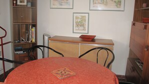 Un comedor con una mesa redonda, sillas, una estantería y obras de arte enmarcadas en la pared.