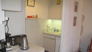 Cocina compacta con cafetera, hervidor y un reloj en la pared.