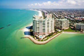 Hotel alto com design curvo, situado perto de uma praia e do oceano, com piscina e áreas ajardinadas.