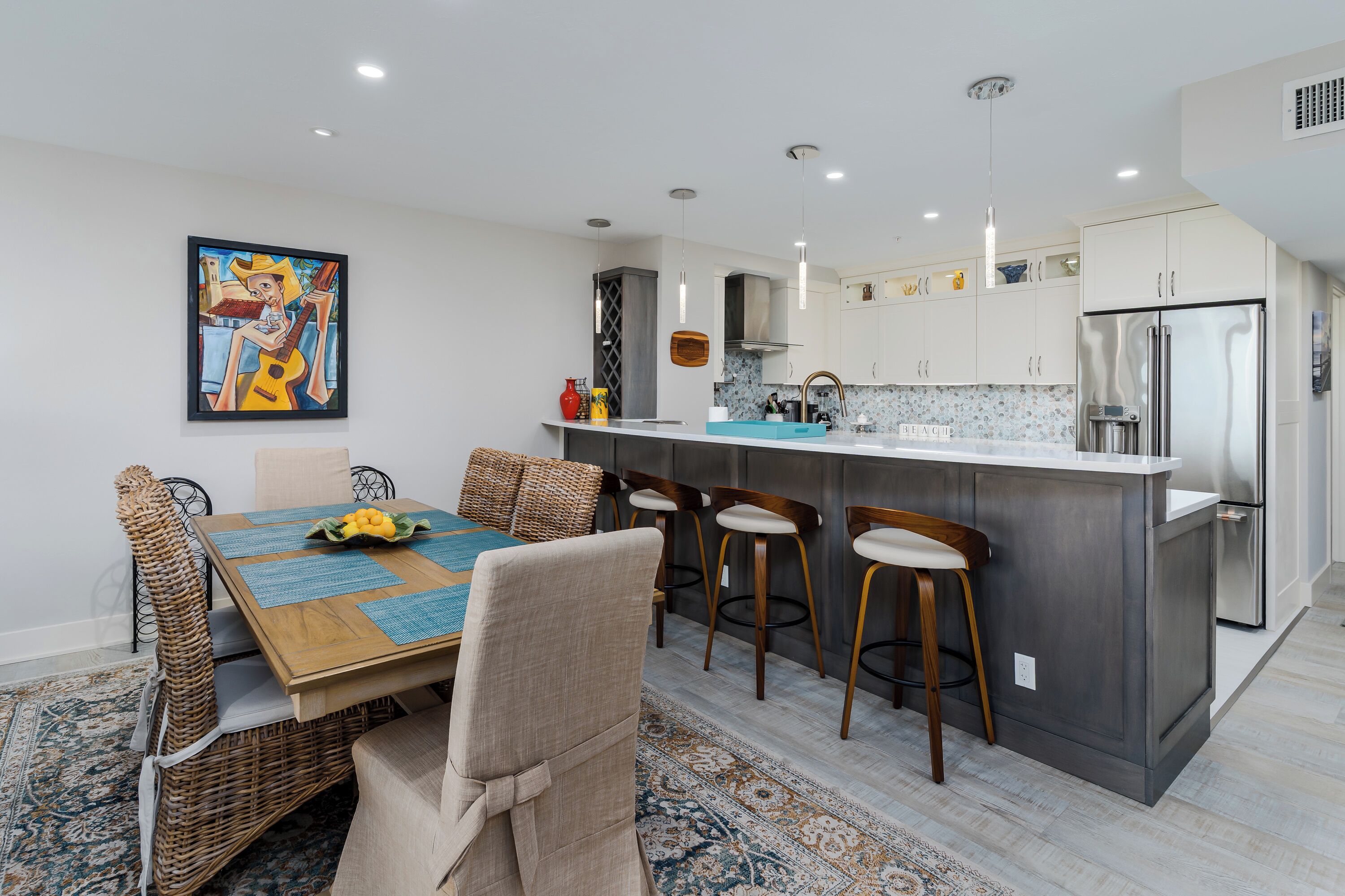 A modern kitchen with a central island, bar stools, and a dining table with chairs.