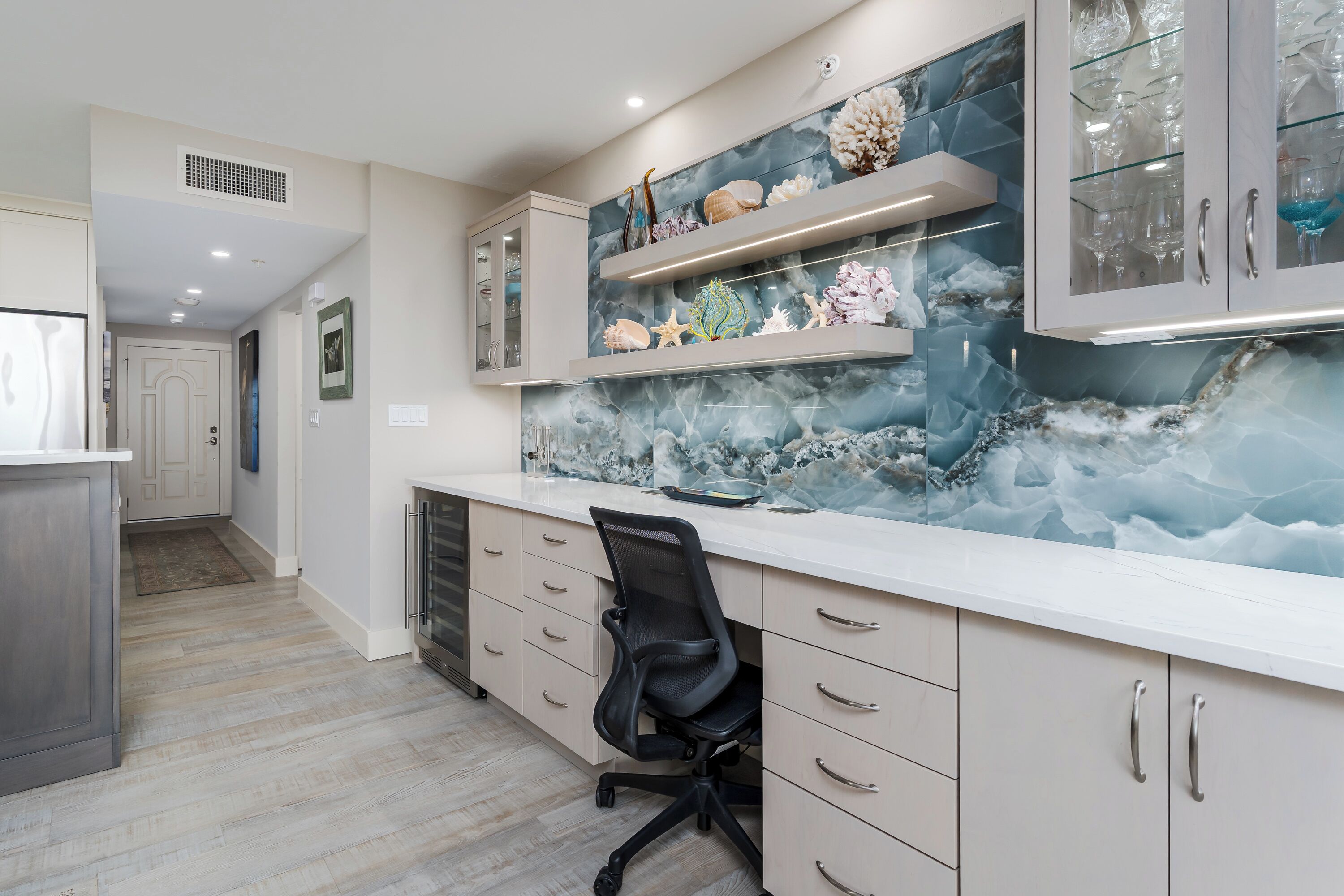 A modern kitchen with marble backsplash, built-in shelves, and a black office chair.