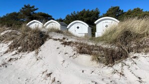 Una fila di casette bianche sulla spiaggia, con tetti curvi, su un terreno sabbioso e scarsamente vegetato.