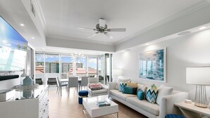 A modern living room with a white sofa, a coffee table, and a ceiling fan. There is a dining area with chairs and a table in the background. - Monthly Executive Picturesque Sunset Retreat (Marco Island)