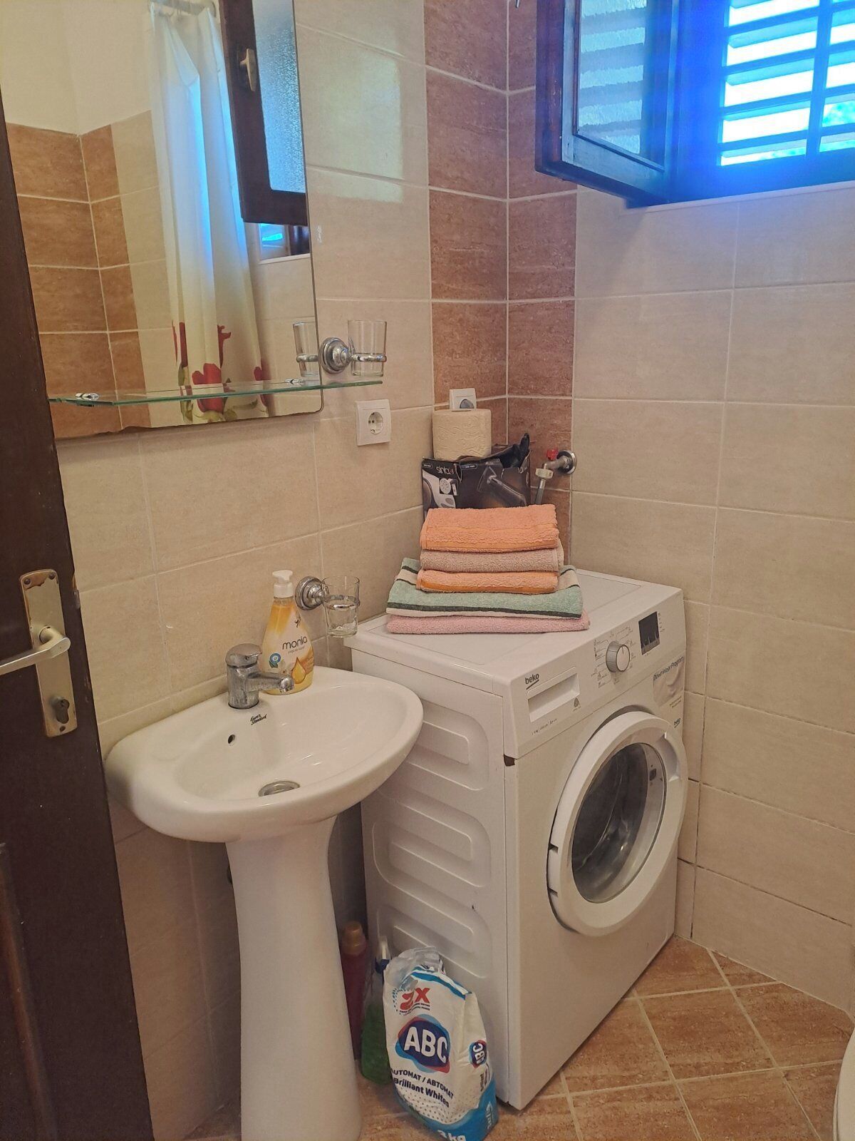 A bathroom with a sink, a washing machine, and a mirror.