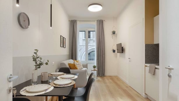 Ein moderner Essbereich mit einem Tisch für vier Personen, einer Couch und Blick auf eine Stadtlandschaft durch ein Fenster.