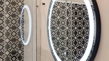 Une salle de bain avec des carreaux décorés et un miroir rond doté d’un cadre lumineux.