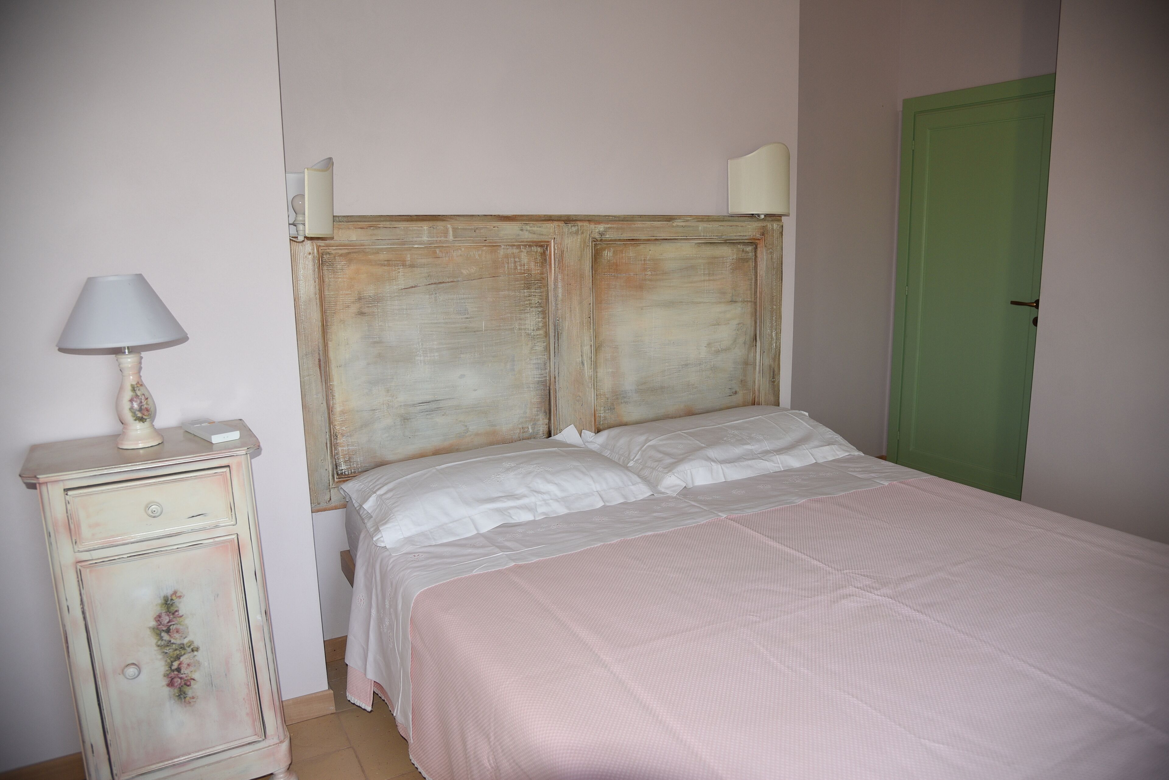 Un dormitorio con una cama, una mesita de noche, una lámpara y una puerta verde.