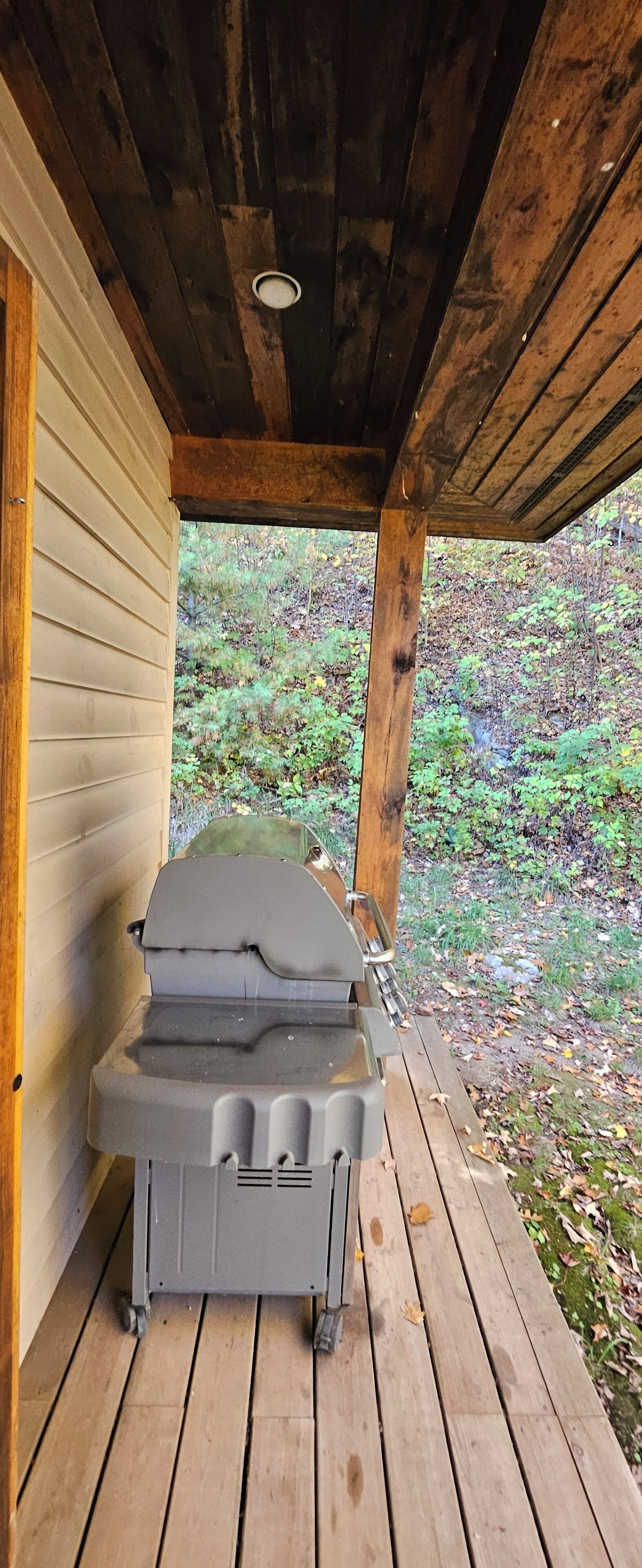 A covered outdoor area with a grill and a wooden deck.