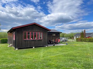 En träbyggnad med ett rött tak, en veranda med stolar och en gräsmatta.