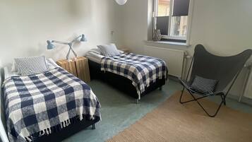 Une chambre avec deux lits, une fenêtre, un radiateur et une chaise.